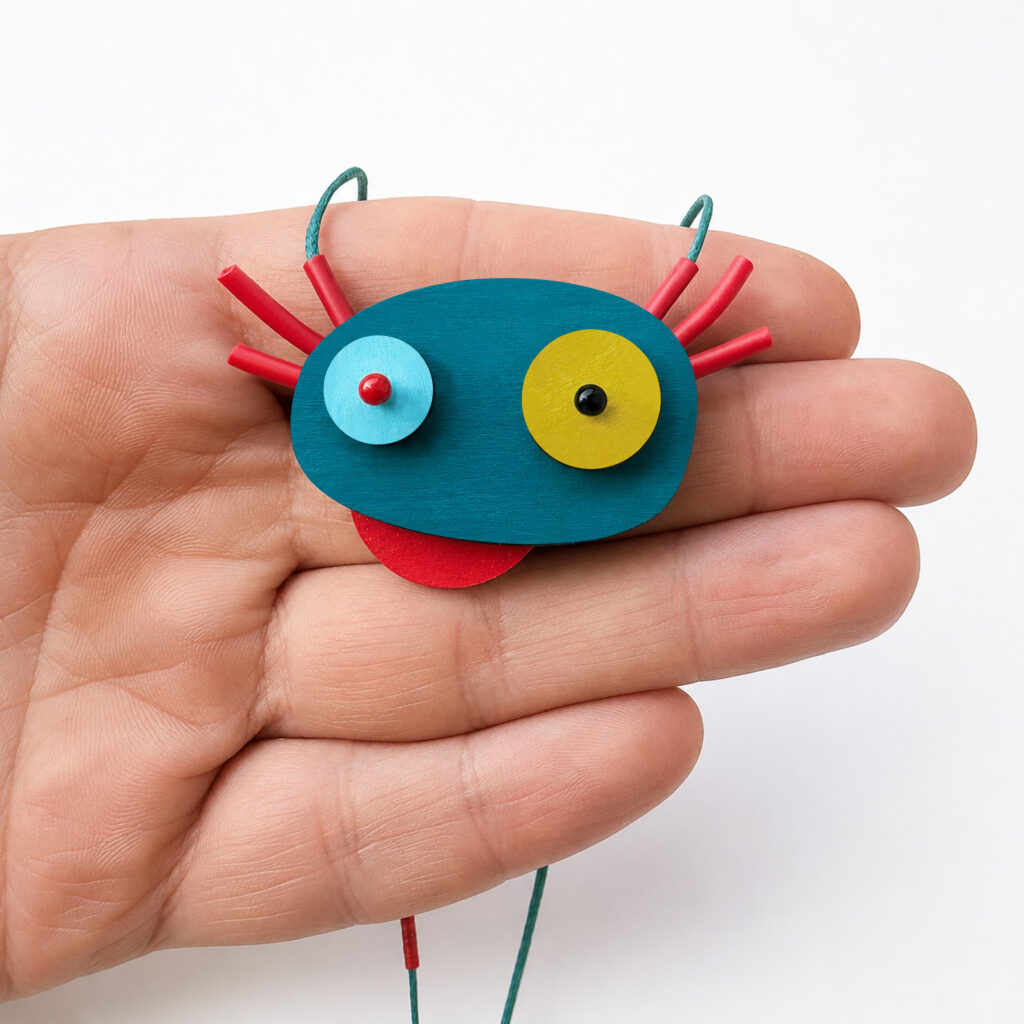 Playful turquoise and red axolotl wooden pendant with colorful circular eyes shown in hand