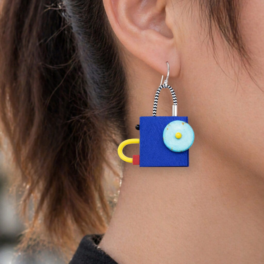 Blue geometric wooden dangle earring with turquoise circle and yellow accent worn on ear