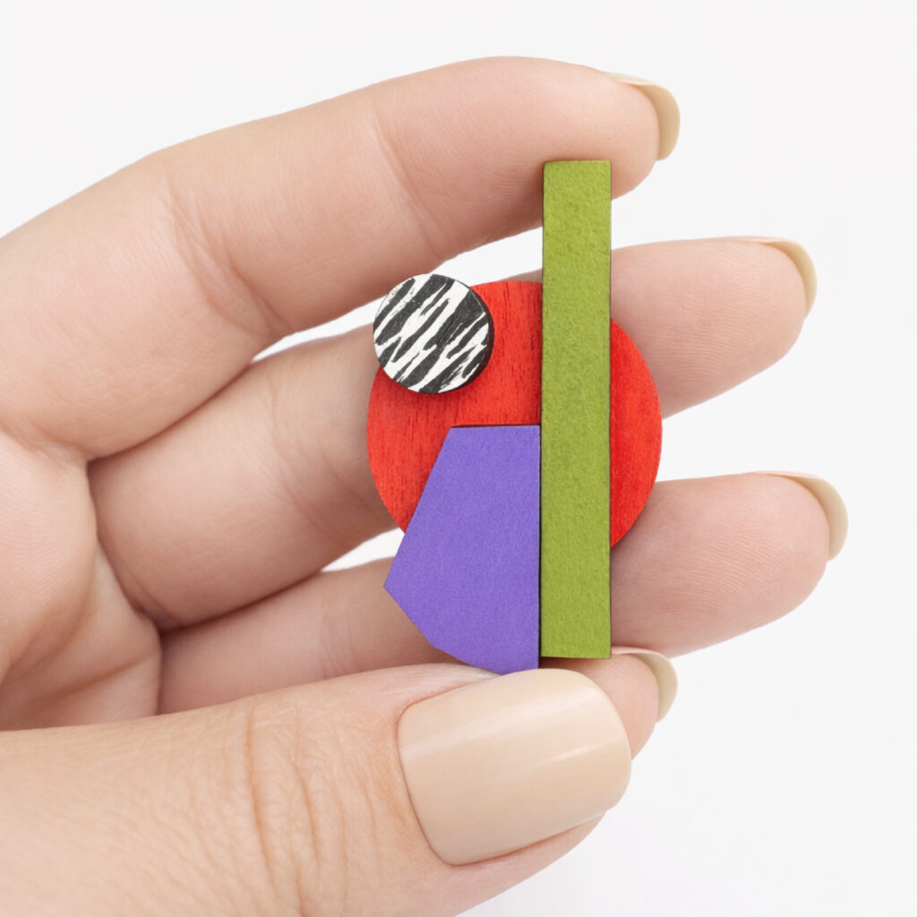 Colorful abstract mismatched wooden earring shown in hand for scale