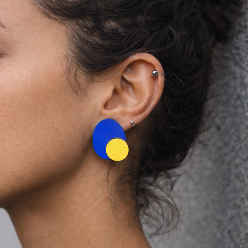 Blue and yellow geometric stud earrings worn on ear