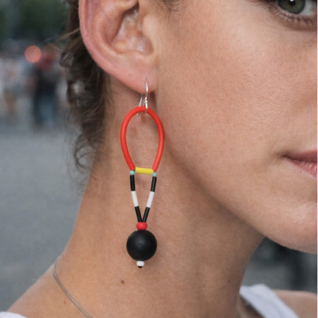 Red and black geometric dangle earring with oval wooden shape and black bead worn on ear