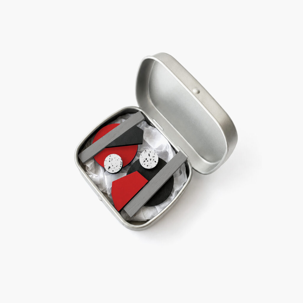 Red black and grey mismatched wooden earrings displayed in a metal gift box