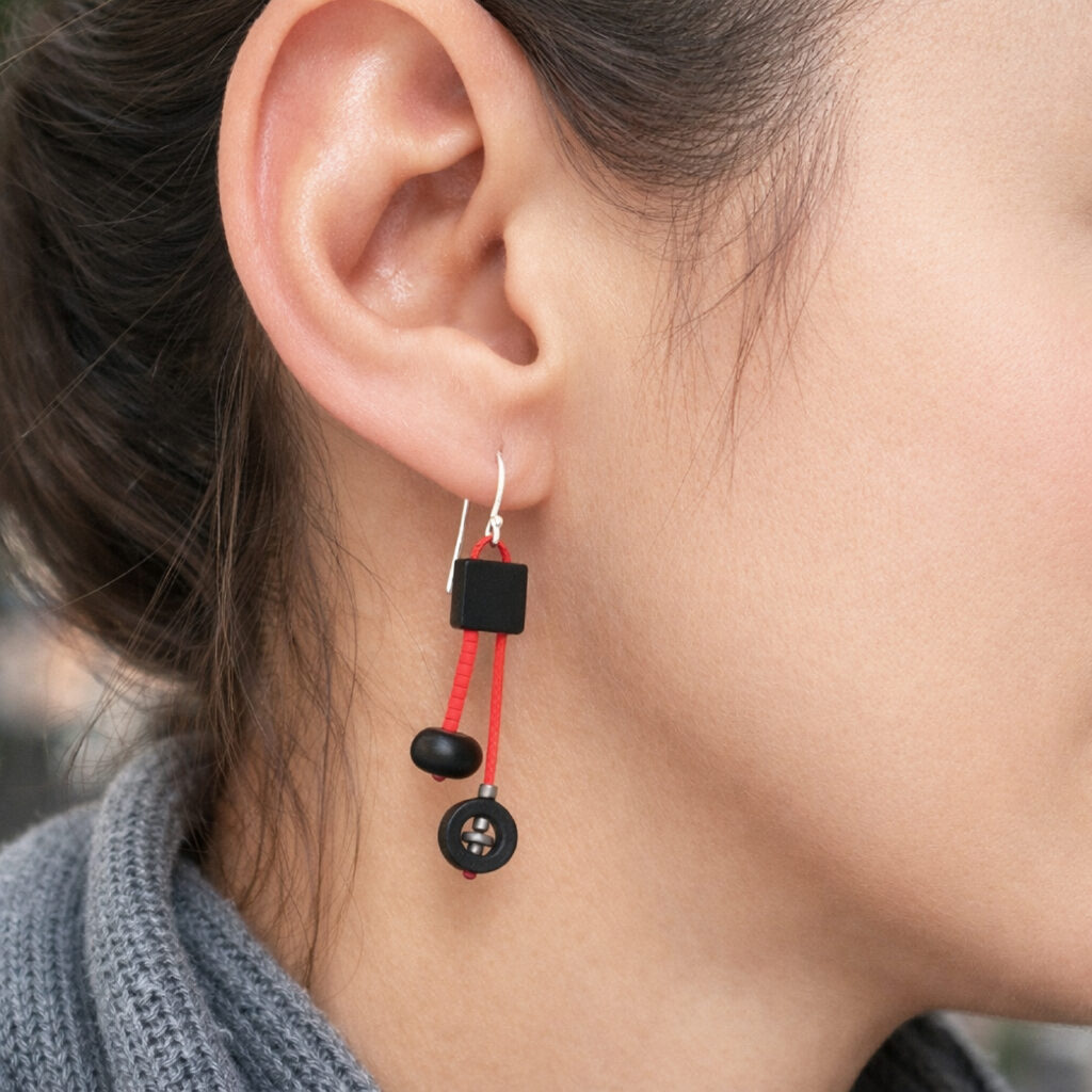 Black and red asymmetrical wooden earring with red cords worn on ear