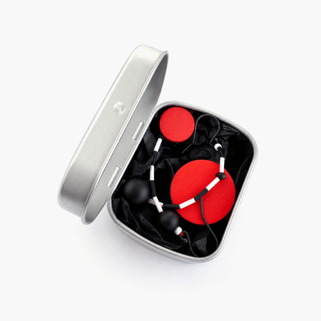 Red and black asymmetrical earrings displayed in a metal gift box