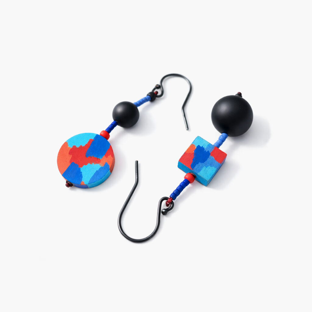 Red and blue abstract geometric earrings with matte black beads shown in hand