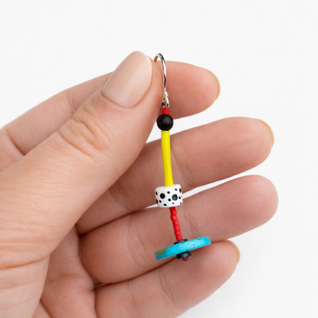 Colorful turquoise and yellow geometric dangle earring with black and white bead held between fingers