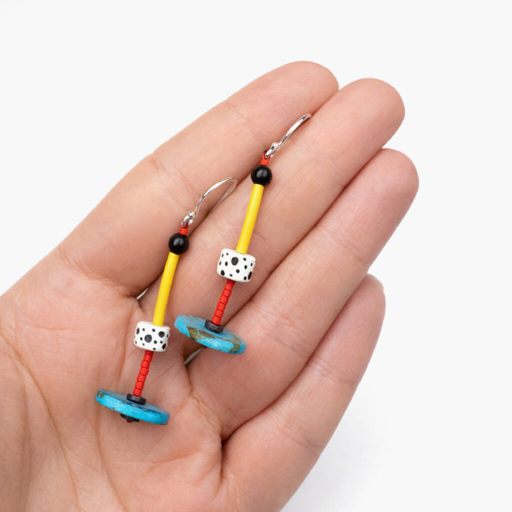 Pair of turquoise red and yellow geometric wooden earrings shown in hand