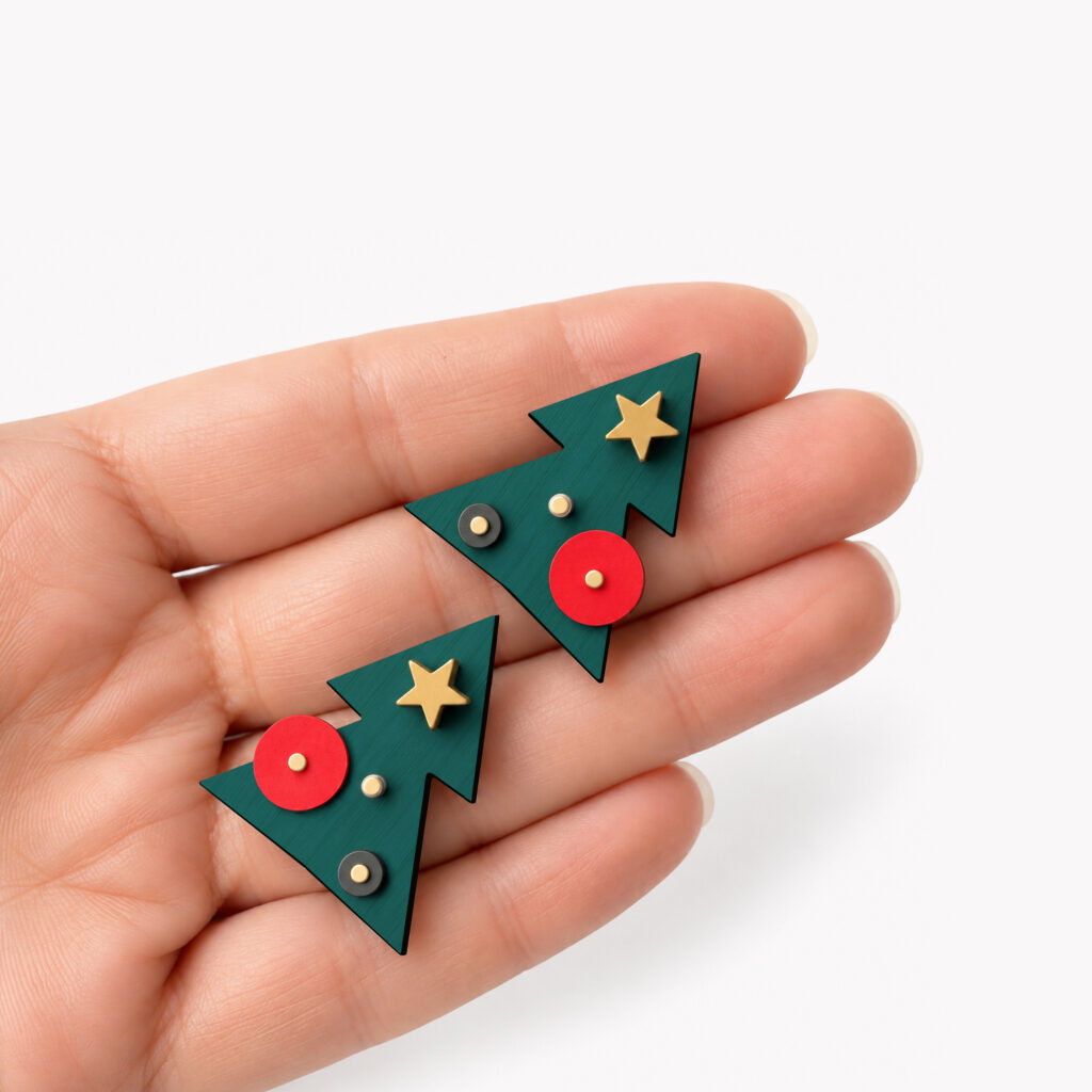 Geometric Christmas tree stud earrings with red ornaments and gold stars shown in hand