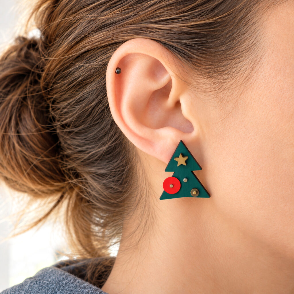 Green Christmas tree stud earring with red and gold decorations worn on ear