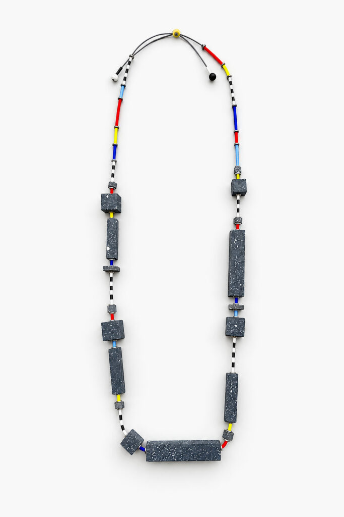 Geometric statement necklace with dark speckled wooden shapes and multicolored accents on a white background