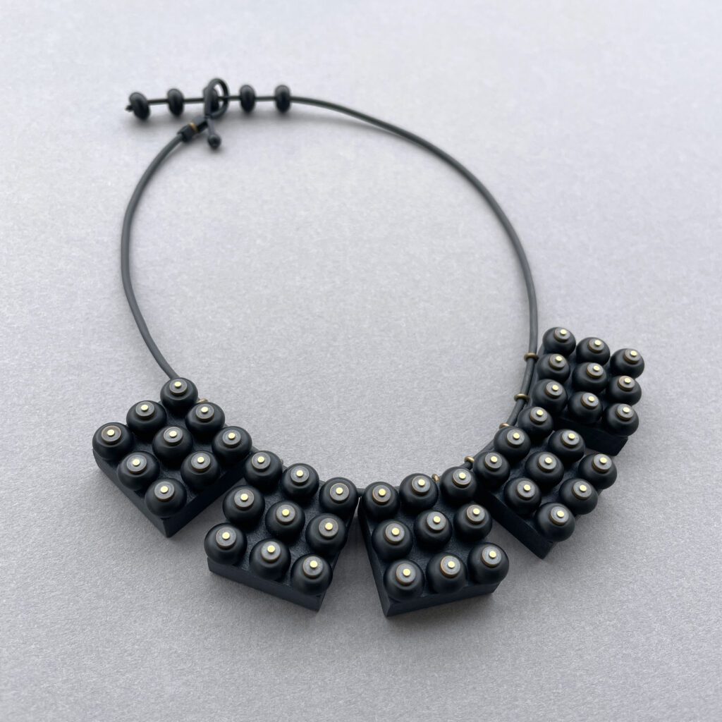 Black geometric statement necklace with sculptural beadwork on grey background